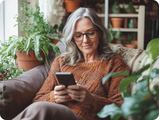 A woman wearing glasses sits on a couch, intently looking at her phone.
